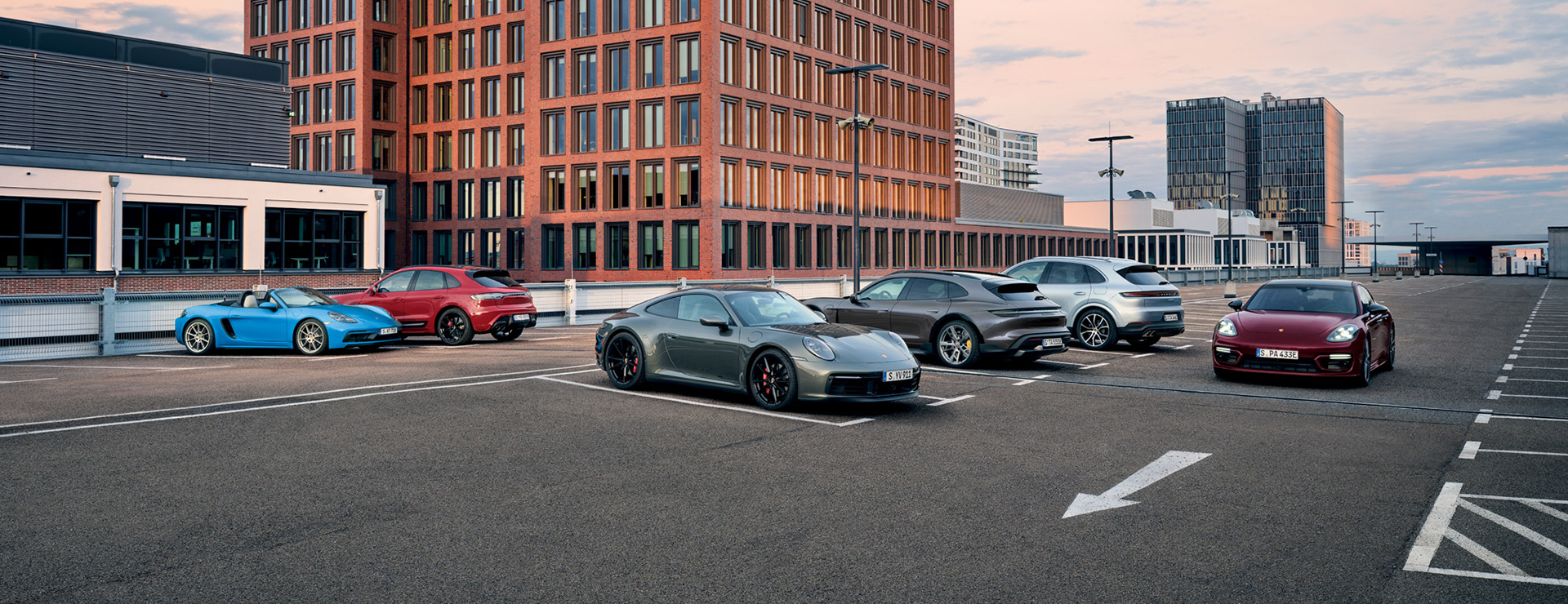 Verschiedene Porsche Modelle auf einem Parkplatz.