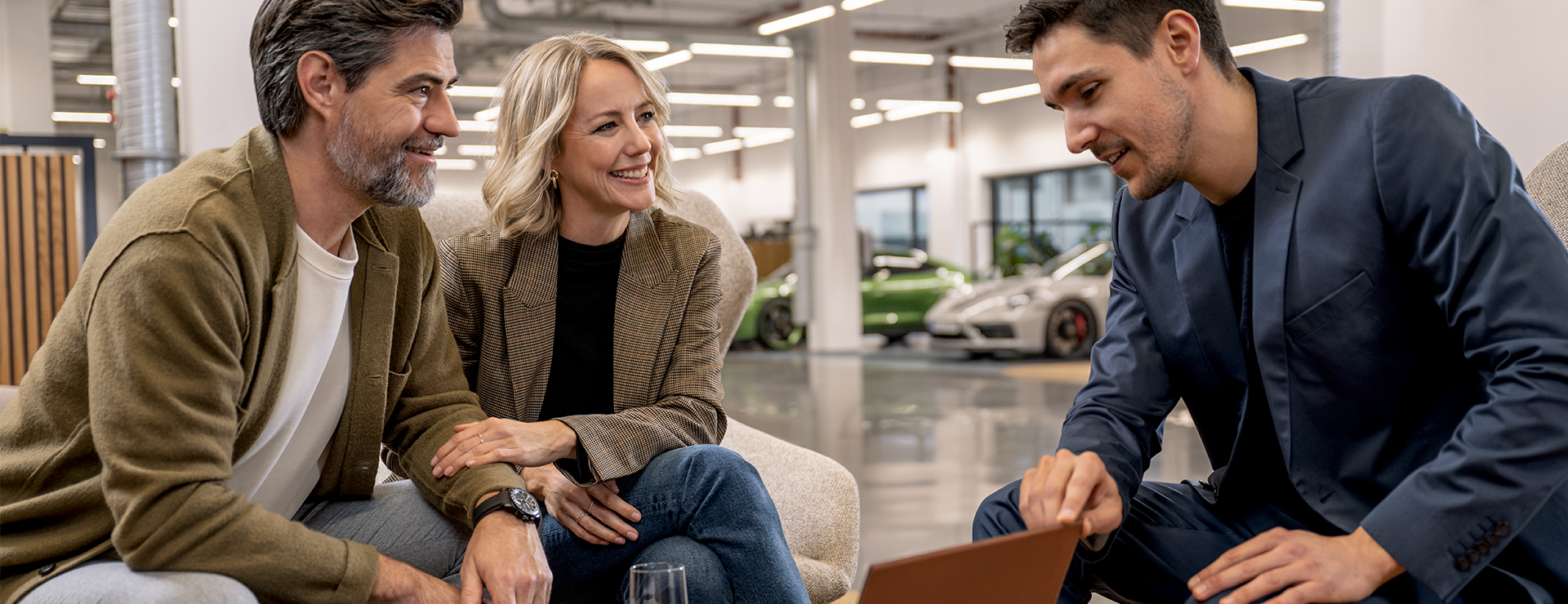 Ein Porsche Kunde und eine Porsche Kundin führen ein Beratungsgespräch mit einem Porsche Mitarbeiter.
